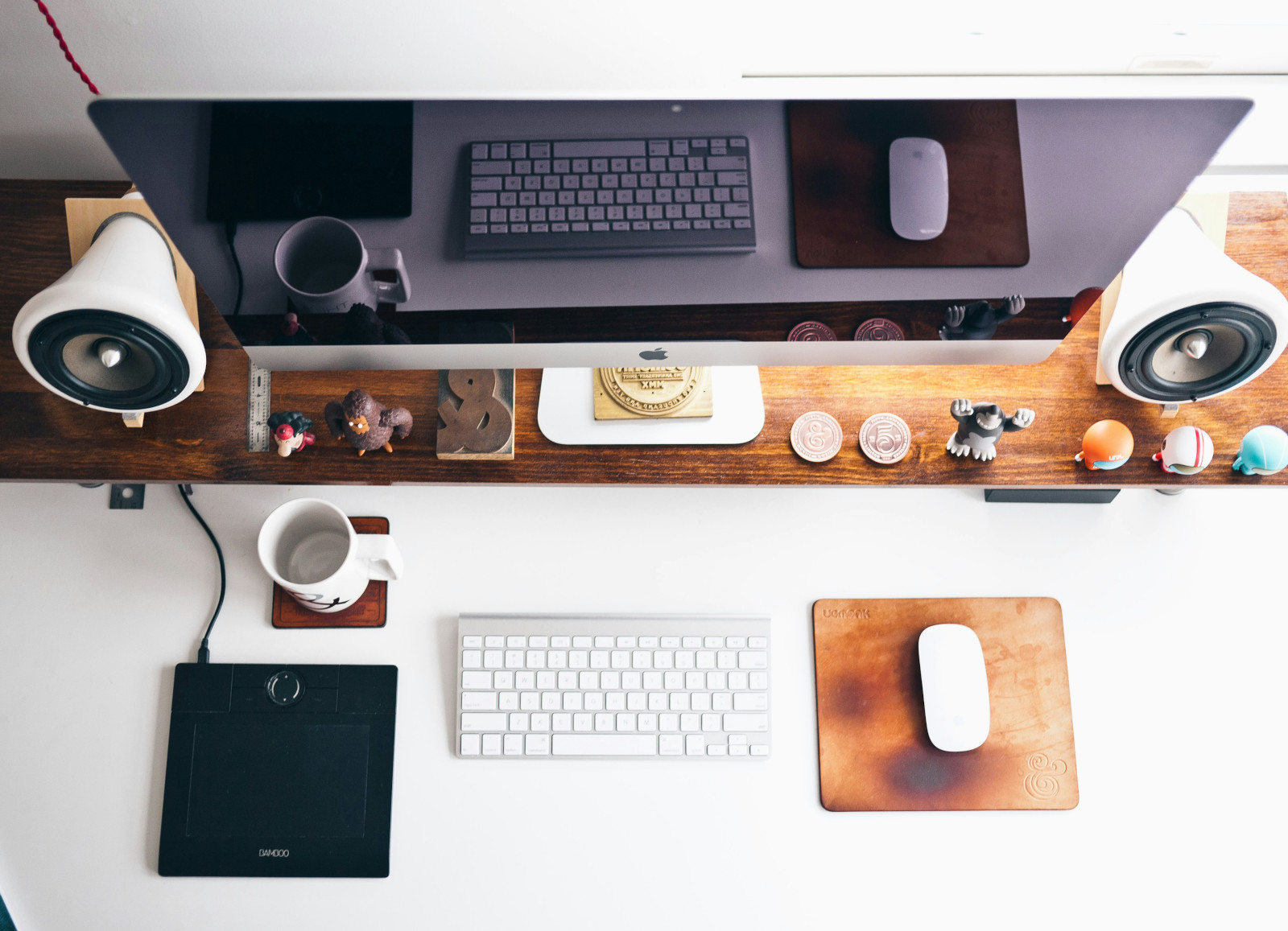 Desk of an administrative assistant that includes a laptop, keyboard, mouse, mug and other desktop items